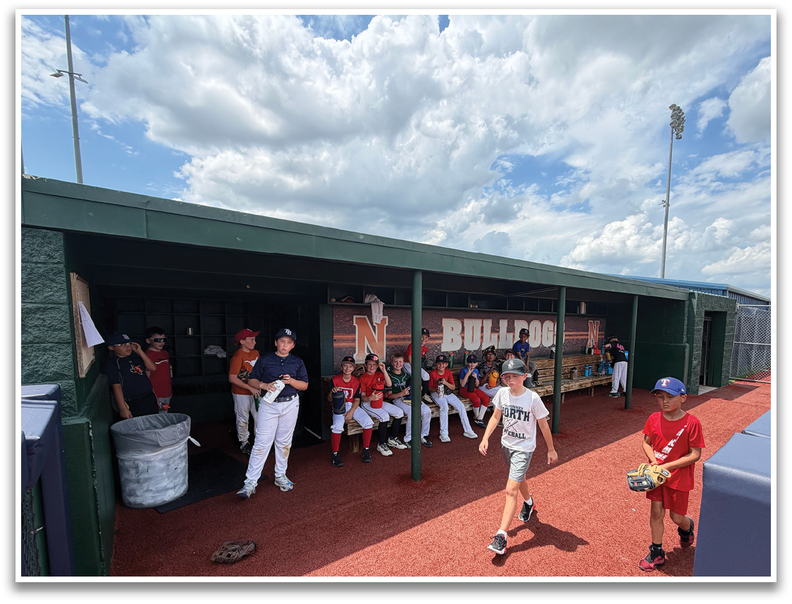 A group of young boys are sitting on a bench in a dugout, watching a baseball game. Contenido generado con IA