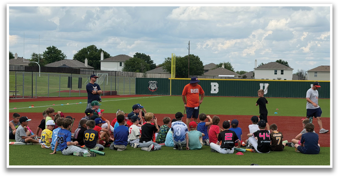 A group of young boys are sitting on a baseball field, listening to a man in an orange shirt. Contenido generado con IA