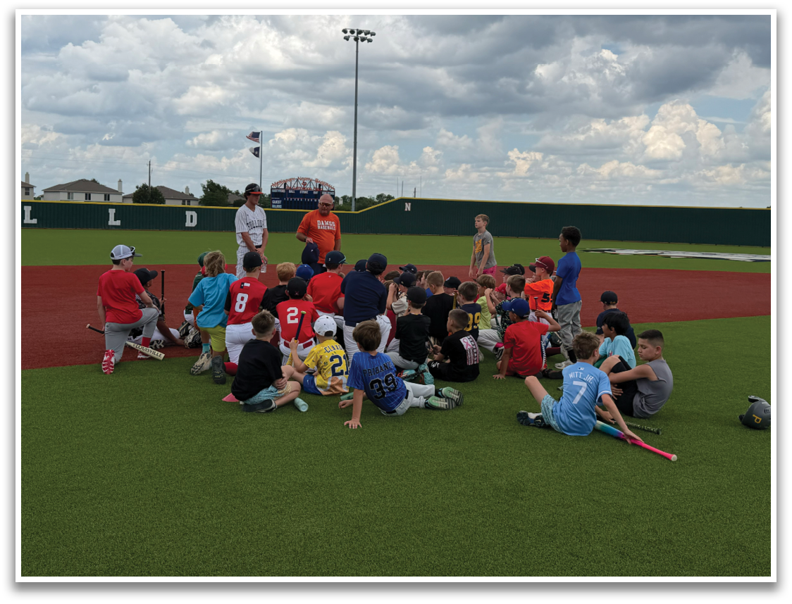 A group of people, including both adults and children, are sitting on the grass in a baseball field. They are gathered around a man who is likely a coach or instructor, possibly discussing a game or learning a new skill. The group is composed of various individuals, some sitting closer to the front and others further back. The scene appears to be a casual, outdoor gathering where people are enjoying the company of others and learning from the man in the center. Contenido generado con IA