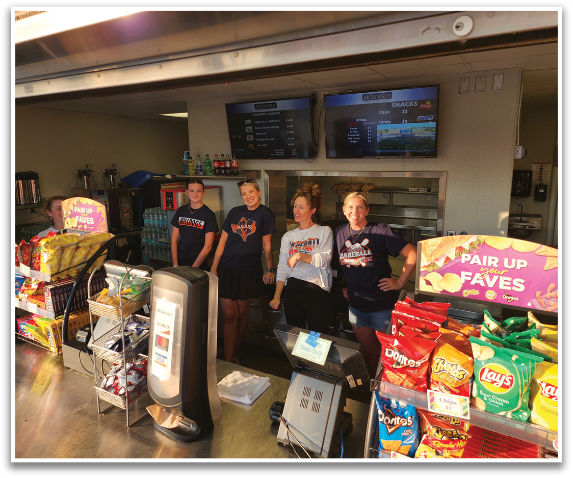 Four women are standing in a food court, posing for a picture. They are surrounded by various snack foods, including chips and soda. Contenido generado con IA