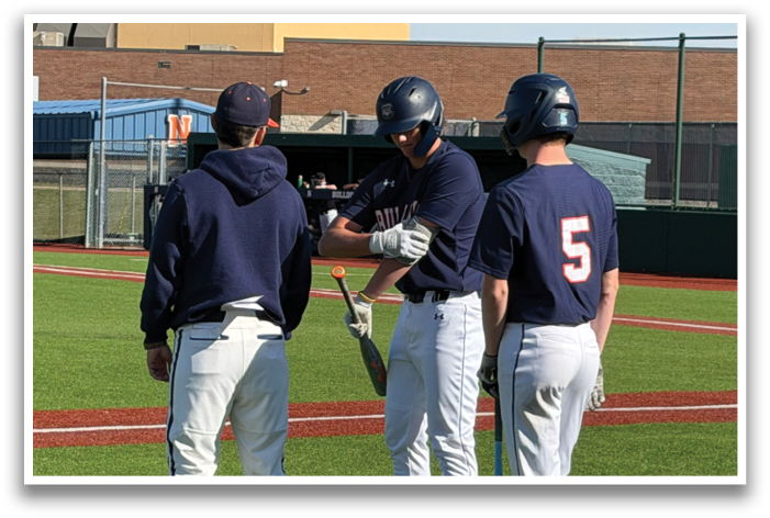Three baseball players on a field, two of them wearing blue shirts and one wearing a red shirt. They are holding baseball bats and talking to each other. Contenido generado con IA