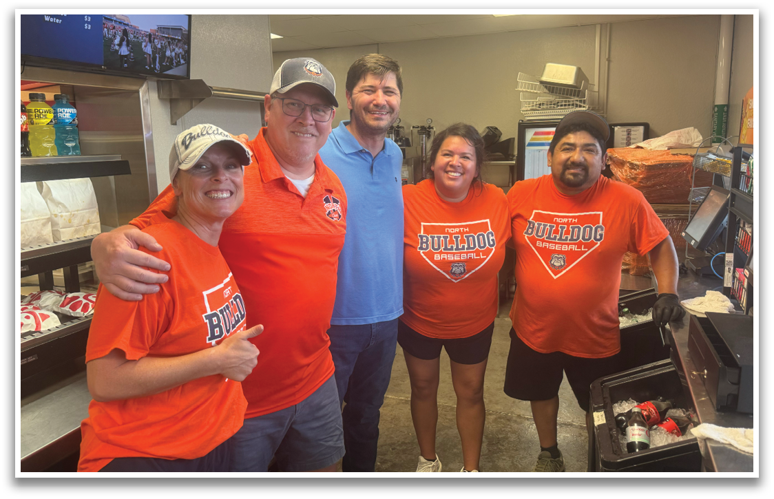 Four people wearing orange shirts pose for a photo in a restaurant. Contenido generado con IA