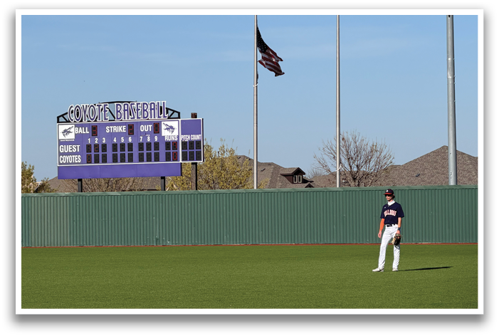 A baseball player stands on a field with a scoreboard in the background. Contenido generado con IA