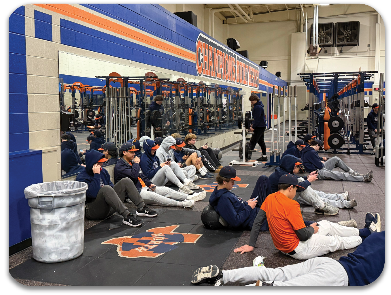 A group of people are sitting on the floor in a gym, resting during a workout. Contenido generado con IA