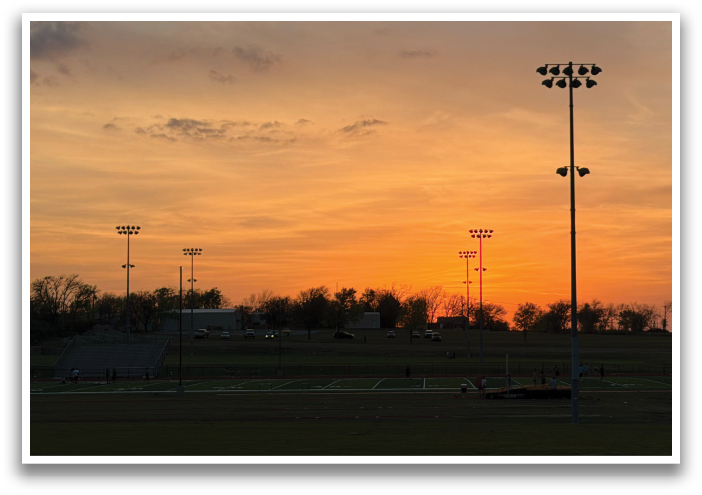 A sunset over a field with a stadium in the background. Contenido generado con IA