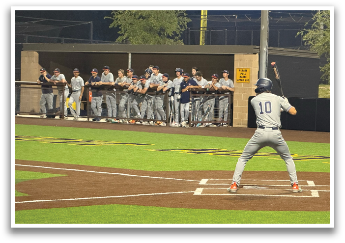 A baseball player is at bat, holding a bat and getting ready to swing. The catcher is positioned behind him, wearing a baseball glove. The scene takes place on a baseball field, with several other players on the field. Contenido generado con IA