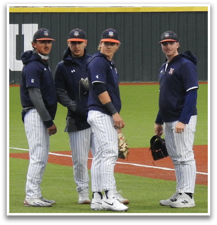 Four baseball players wearing blue and grey uniforms stand on a field. Contenido generado con IA