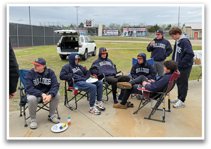 A group of people are sitting in chairs on a sidewalk, eating and drinking. There are several cups and a bottle on the ground near them. A truck is parked nearby. Contenido generado con IA