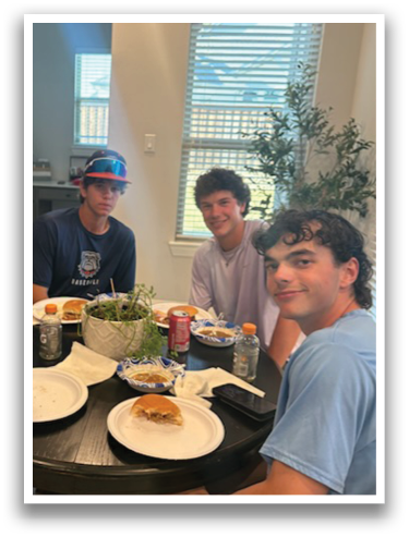 Four young men are sitting around a table with plates of food, enjoying a meal together. Contenido generado con IA