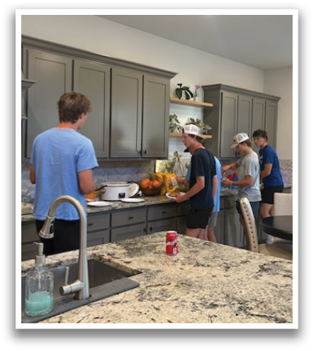 A group of people are gathered in a kitchen, preparing food. There are several oranges on the counter, and a cup is placed nearby. The kitchen is equipped with a sink, oven, and refrigerator. A dining table is also present in the room. Contenido generado con IA
