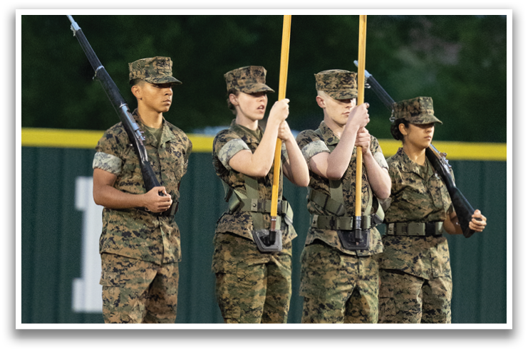 Three soldiers in camouflage uniforms are standing on a baseball field, holding an American flag. Contenido generado con IA