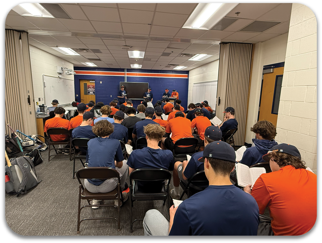 A group of men wearing orange shirts are sitting in a room, reading books. Contenido generado con IA