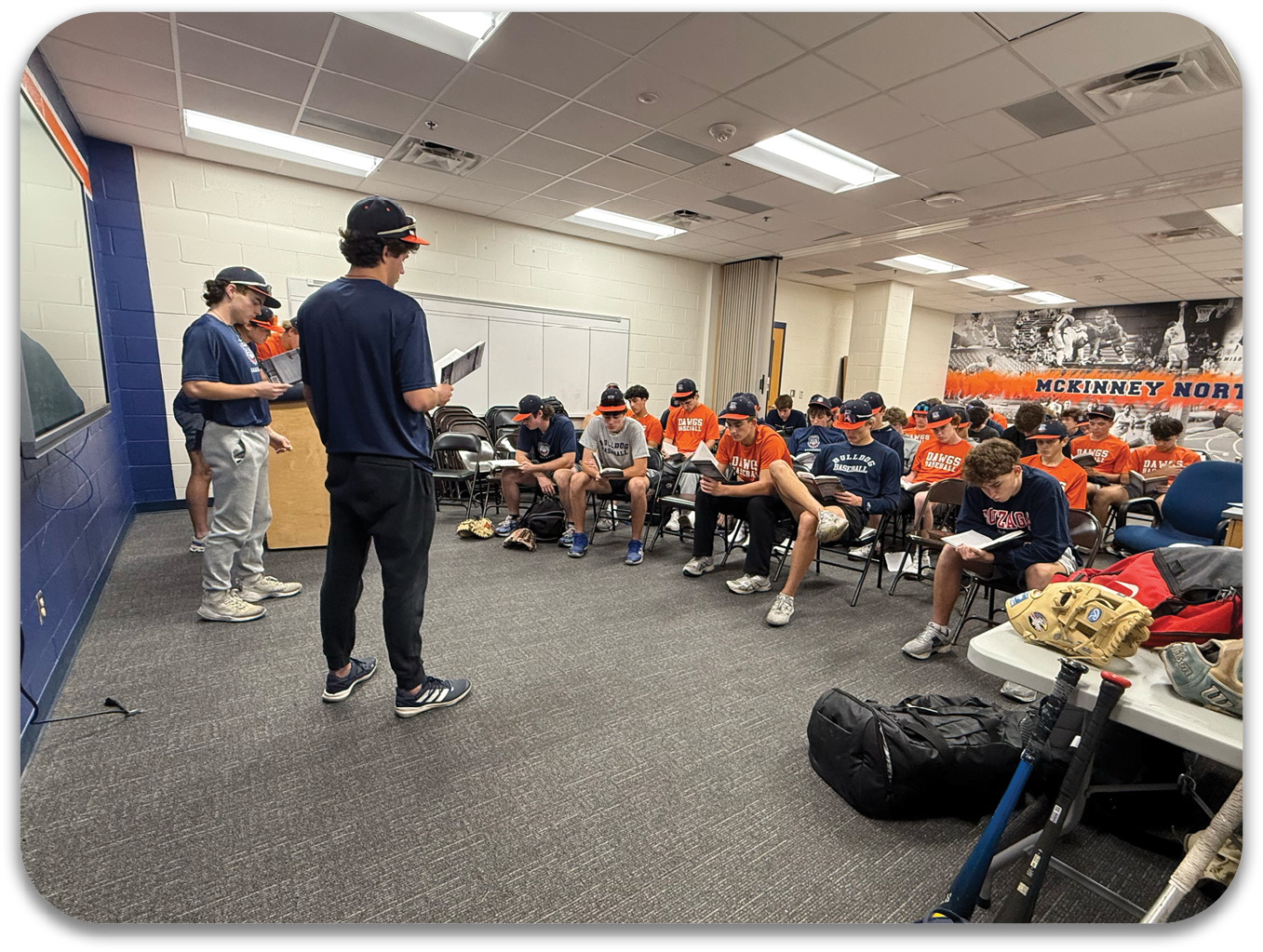 A group of baseball players are sitting in a room, some of them wearing helmets. Contenido generado con IA
