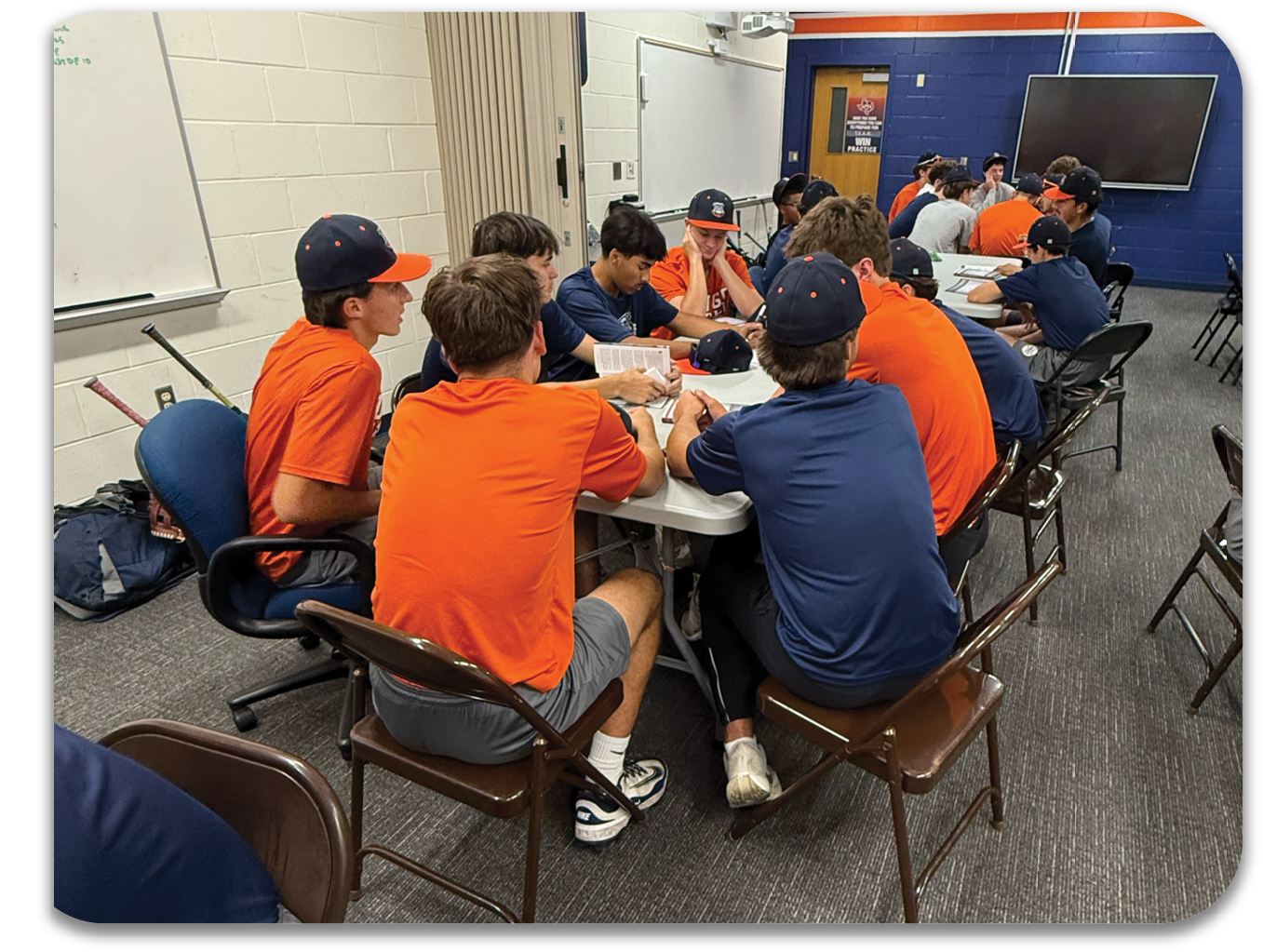 A group of men wearing orange shirts are sitting around a table in a room. Contenido generado con IA