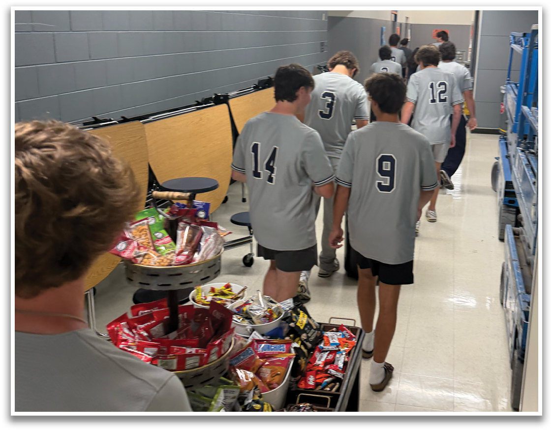 A group of people are standing in a hallway, looking at a table filled with snacks. Contenido generado con IA