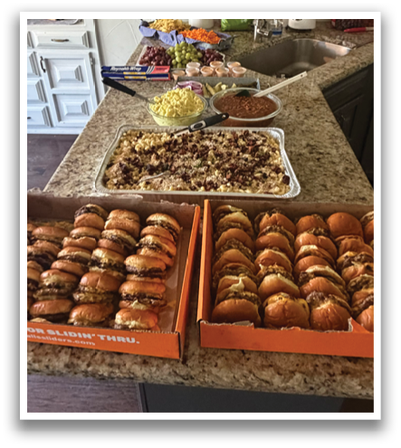 A table is filled with various food items, including sandwiches and a bowl of food. The table is also covered with several bottles. The scene appears to be a buffet or a gathering where people can serve themselves. Contenido generado con IA