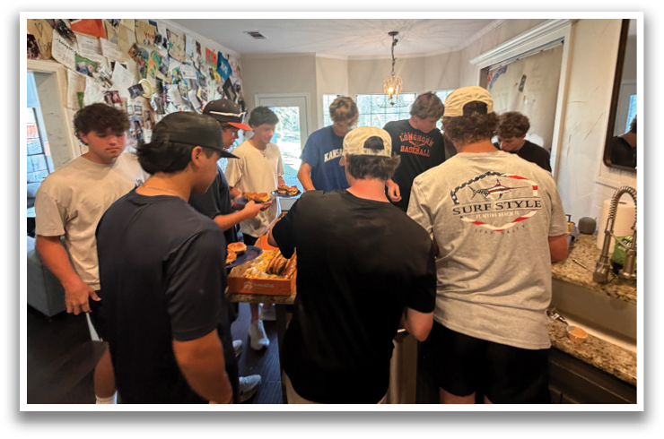 A group of people are gathered in a kitchen, preparing food. They are wearing baseball caps and shirts. Contenido generado con IA