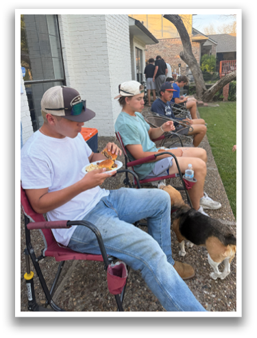 A group of people are sitting outside on chairs, eating and drinking. A dog is also present, sitting on the ground near the people. Contenido generado con IA