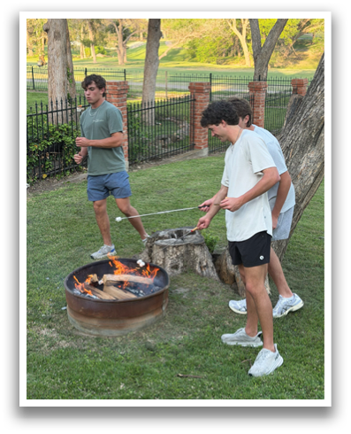 Two men are standing in a grassy area, one of them holding a frisbee. They are near a fire pit, and there is a fence in the background. Contenido generado con IA