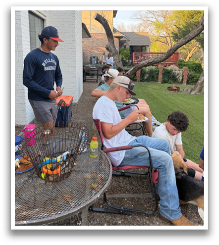 A group of people are sitting outside on a patio, enjoying the sunny day. They are sitting on chairs and a bench, with some of them holding beverages. There are also a few dogs present, one of which is on a leash. Contenido generado con IA