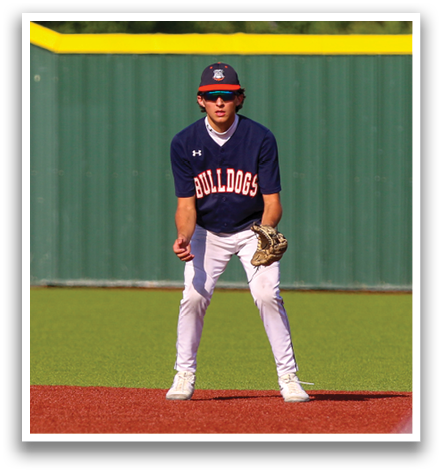 A baseball player wearing a blue and red shirt and white pants is standing on the field. Contenido generado con IA