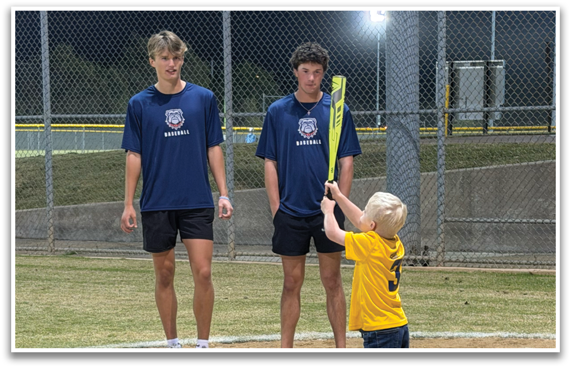 Three children are standing on a baseball field, each holding a baseball bat. They are positioned in a line, with one child closer to the left, another in the middle, and the third on the right. The children are likely practicing their batting skills or participating in a game. Contenido generado con IA