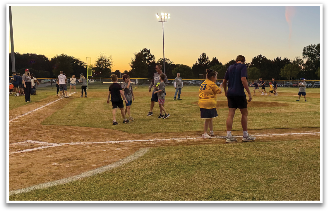 A group of people, including a man and a woman, are standing on a baseball field. The woman is wearing a yellow shirt. Contenido generado con IA