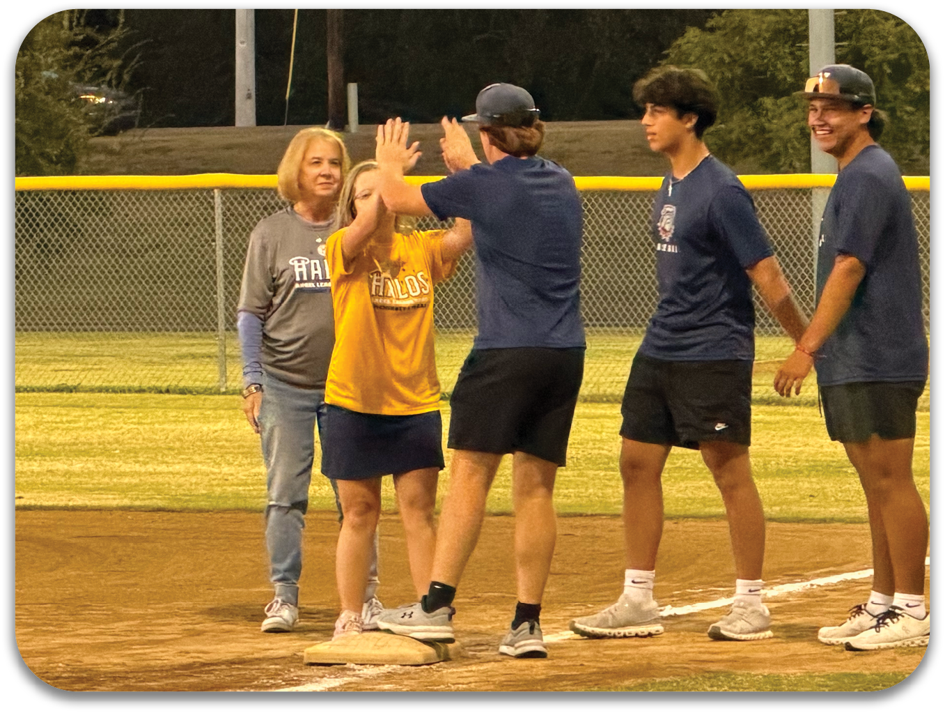 A group of people are standing on a baseball field, with one person in a yellow shirt waving to the camera. Contenido generado con IA
