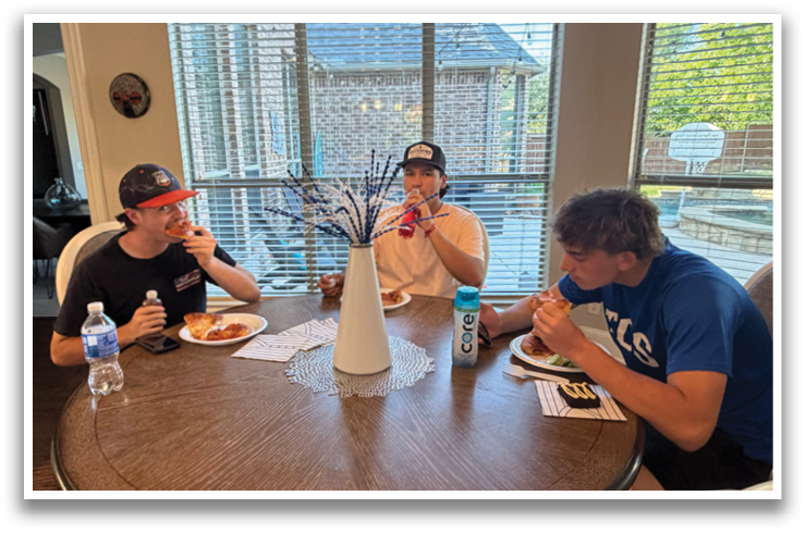 Three people are sitting around a dining table, enjoying a meal together. They have plates of food in front of them, and there are bottles and cups on the table as well. The table is surrounded by chairs, and the room has a window that allows natural light to enter. Contenido generado con IA