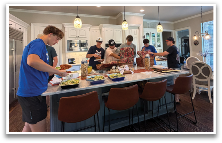A group of people are gathered in a kitchen, preparing food and enjoying each other's company. There are several chairs and a dining table in the room, with a refrigerator and an oven visible in the background. The people are engaged in conversation and laughter, creating a warm and inviting atmosphere. Contenido generado con IA