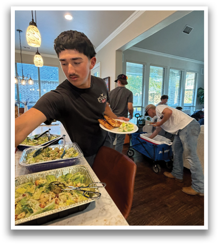 A group of people are standing around a dining table with plates of food. Contenido generado con IA