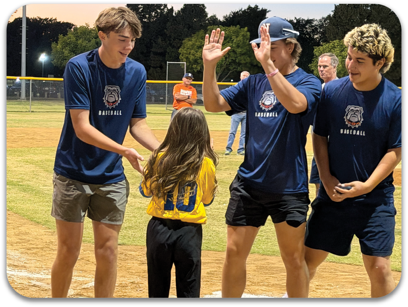 Three men and a girl are on a baseball field. The girl is wearing a yellow jersey and the men are wearing blue shirts. The men are holding up their hands in the air. Contenido generado con IA