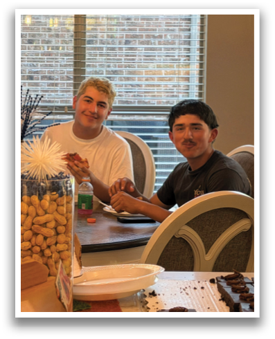 Three men are sitting around a dining table, enjoying a meal together. The table is set with plates, cups, and bowls, and there are several bottles and oranges on the table as well. The men are smiling and appear to be having a good time. Contenido generado con IA