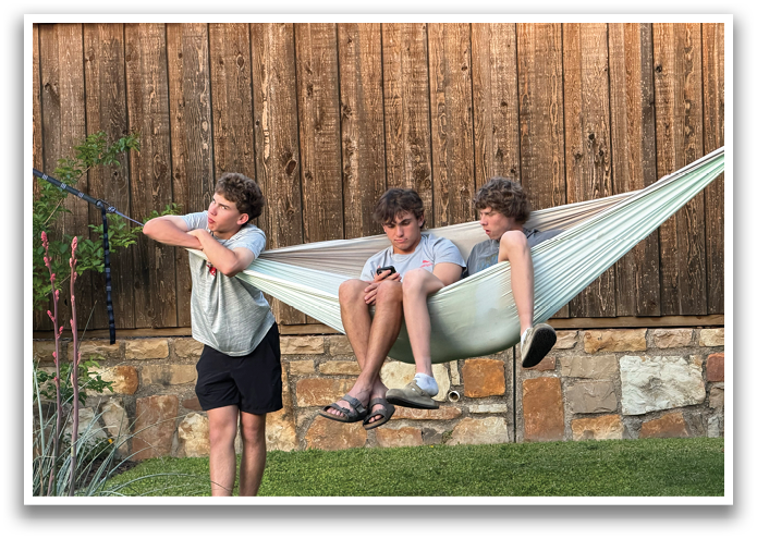 Three young men are sitting in a hammock, one of them holding a cell phone. Contenido generado con IA