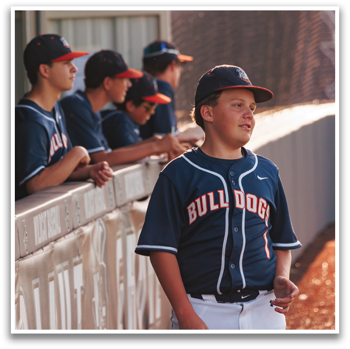 A young boy wearing a baseball uniform stands on a baseball field. Contenido generado con IA