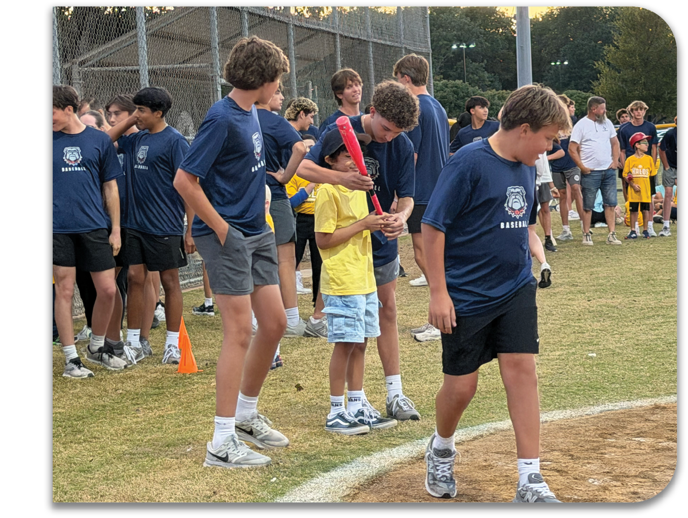 A group of young people, including children, are standing on a baseball field. They are holding baseball bats and wearing blue shirts. Contenido generado con IA