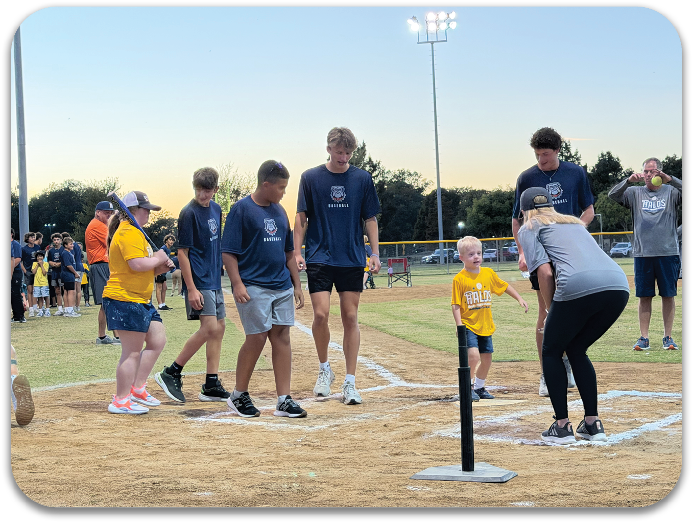A group of people, including children, are playing baseball on a field. A woman is bending over to help a young boy with his baseball swing. Contenido generado con IA