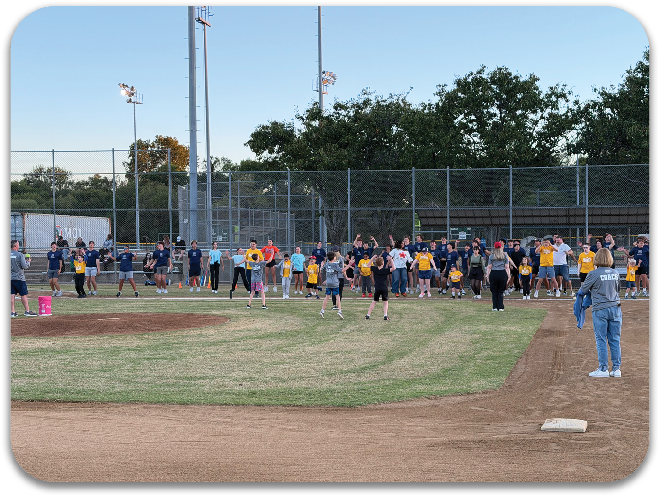 A large group of people are standing on a baseball field, some of them wearing baseball gloves. They are gathered around a base, possibly participating in a baseball game or practice. Contenido generado con IA