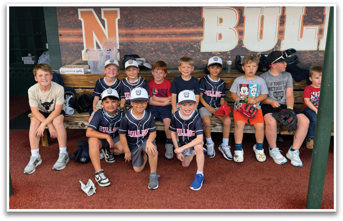 A group of children wearing baseball uniforms are sitting on a bench. Contenido generado con IA