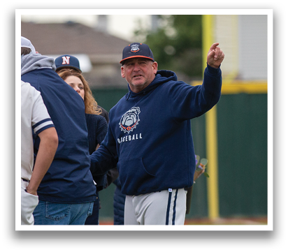 A man wearing a blue and white hoodie stands on a baseball field, pointing at something. Contenido generado con IA