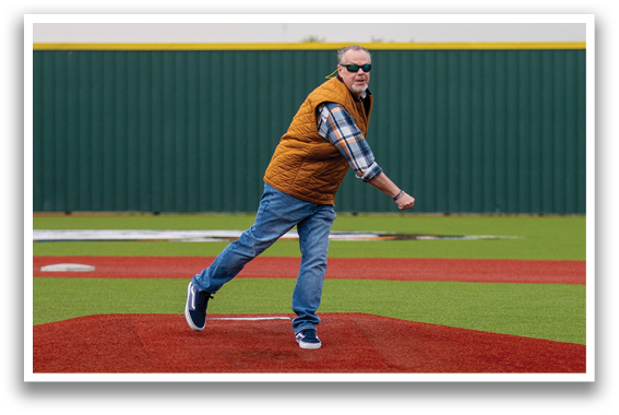 A man in a yellow vest is throwing a baseball on a baseball field. Contenido generado con IA
