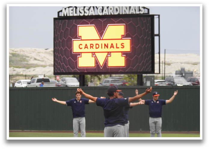 A group of men are standing on a field, forming a circle and raising their arms. They are wearing blue shirts and are facing a large sign. Contenido generado con IA