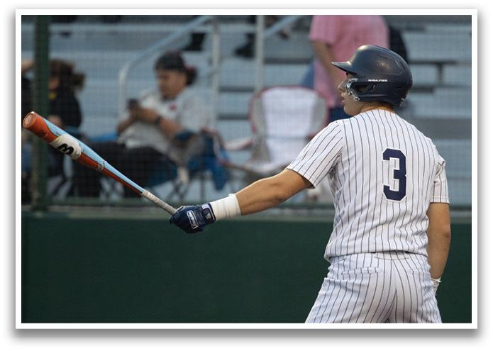 A baseball player in a blue helmet and white uniform is holding a bat and standing on a baseball field. Contenido generado con IA
