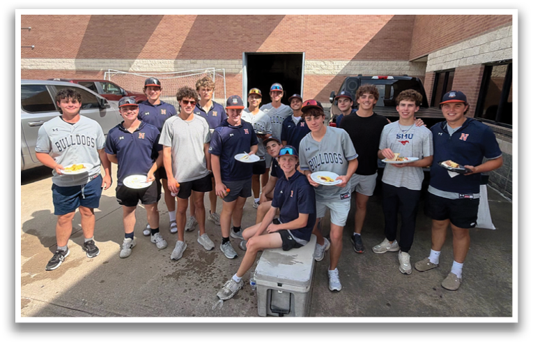 A group of young men in a brick building, some wearing baseball caps, pose for a picture with plates of food in their hands. Contenido generado con IA