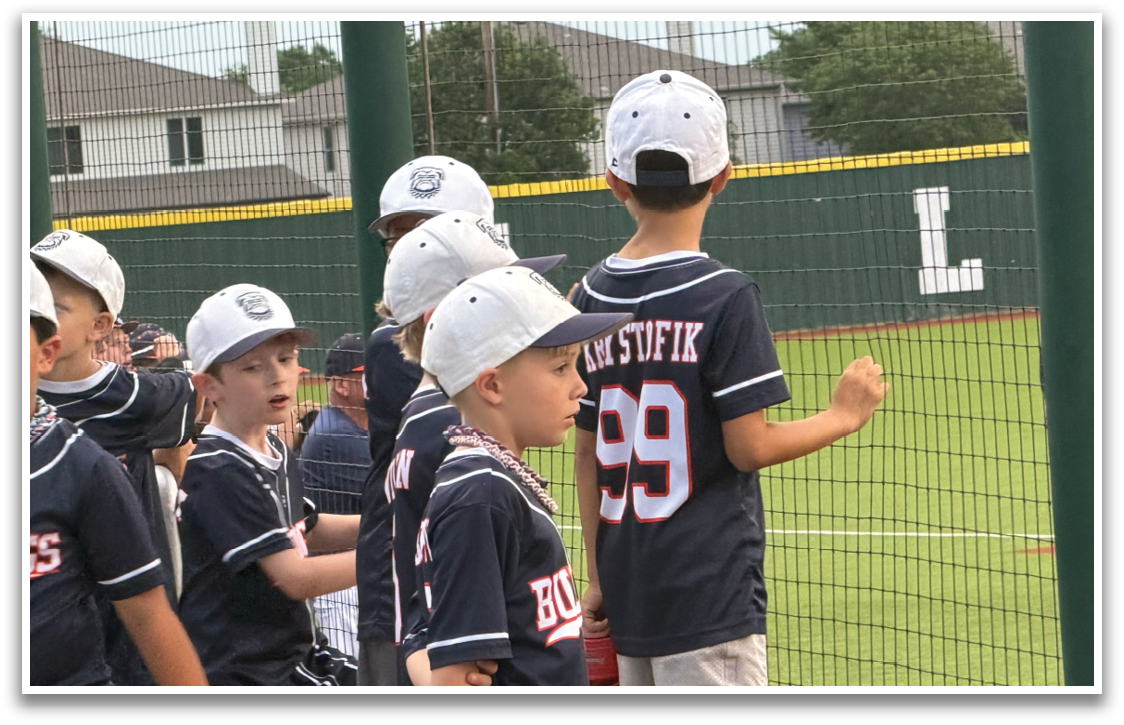 A group of young boys wearing blue baseball uniforms are standing on a baseball field. Contenido generado con IA