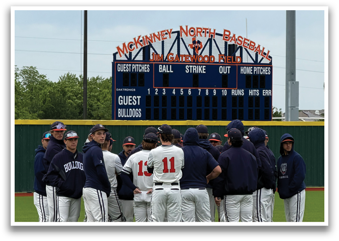 A group of baseball players are standing on the field, wearing blue and red uniforms. They are gathered in front of a scoreboard, possibly waiting for their turn to play or taking a break. The scene is set on a grassy field, and the players are standing in a line, facing the scoreboard. Contenido generado con IA