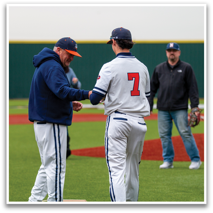 Two men shake hands on a baseball field, one wearing a blue jacket and the other wearing a white and blue uniform. Contenido generado con IA