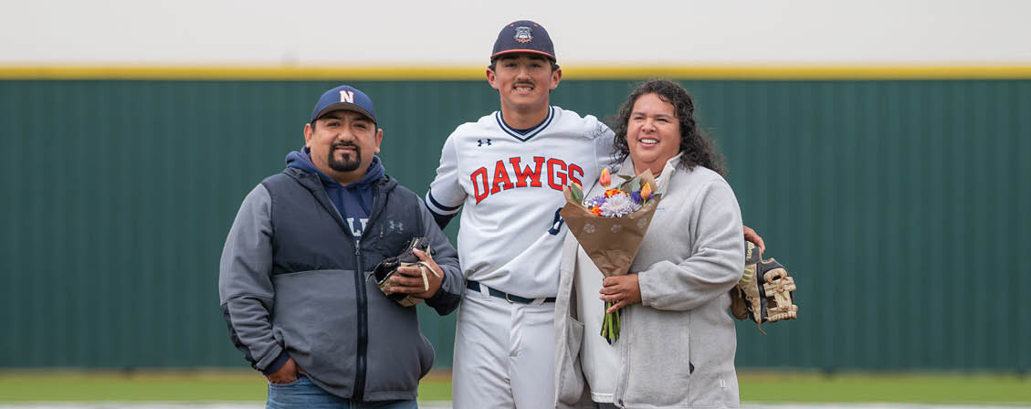 A man, woman, and another person are standing on a baseball field. The man is wearing a baseball uniform and holding a bouquet of flowers. Contenido generado con IA