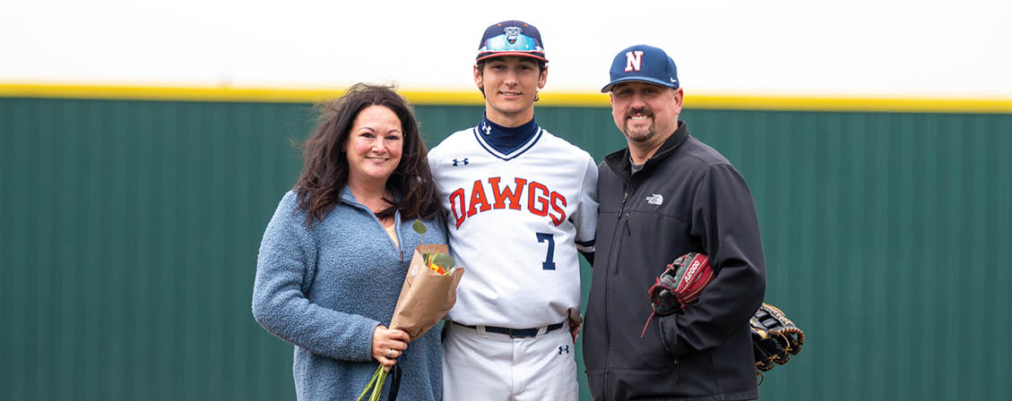 A man and woman pose for a picture on a baseball field with the man wearing a baseball uniform. Contenido generado con IA
