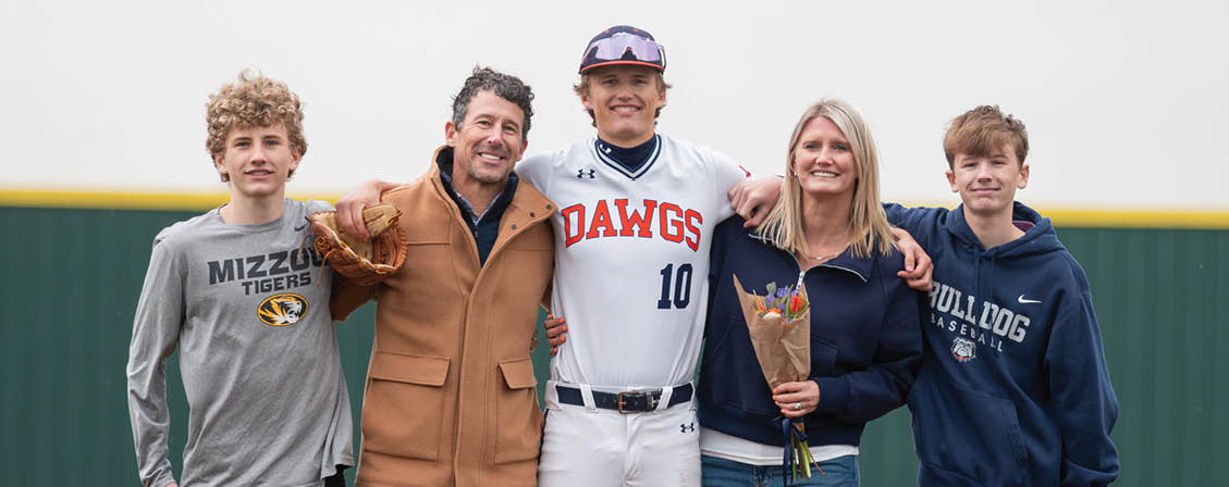 A group of people, including a baseball player, pose for a picture on a baseball field. Contenido generado con IA